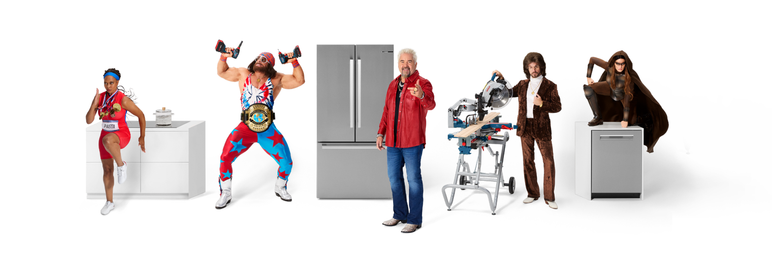 A group shot showcasing the five Like A Bosch heroes. Featuring Guy Fieri next to the Bosch fridge, Macho Man Randy Savage holding two 18V 2-in-1 Impact drivers, the fastest springer lady next to her induction cooktop from Bosch. On the left side we see the smoothest guy on the construction side with his 18V Glide Miter Saw followed by our hero on the Bosch dishwasher.